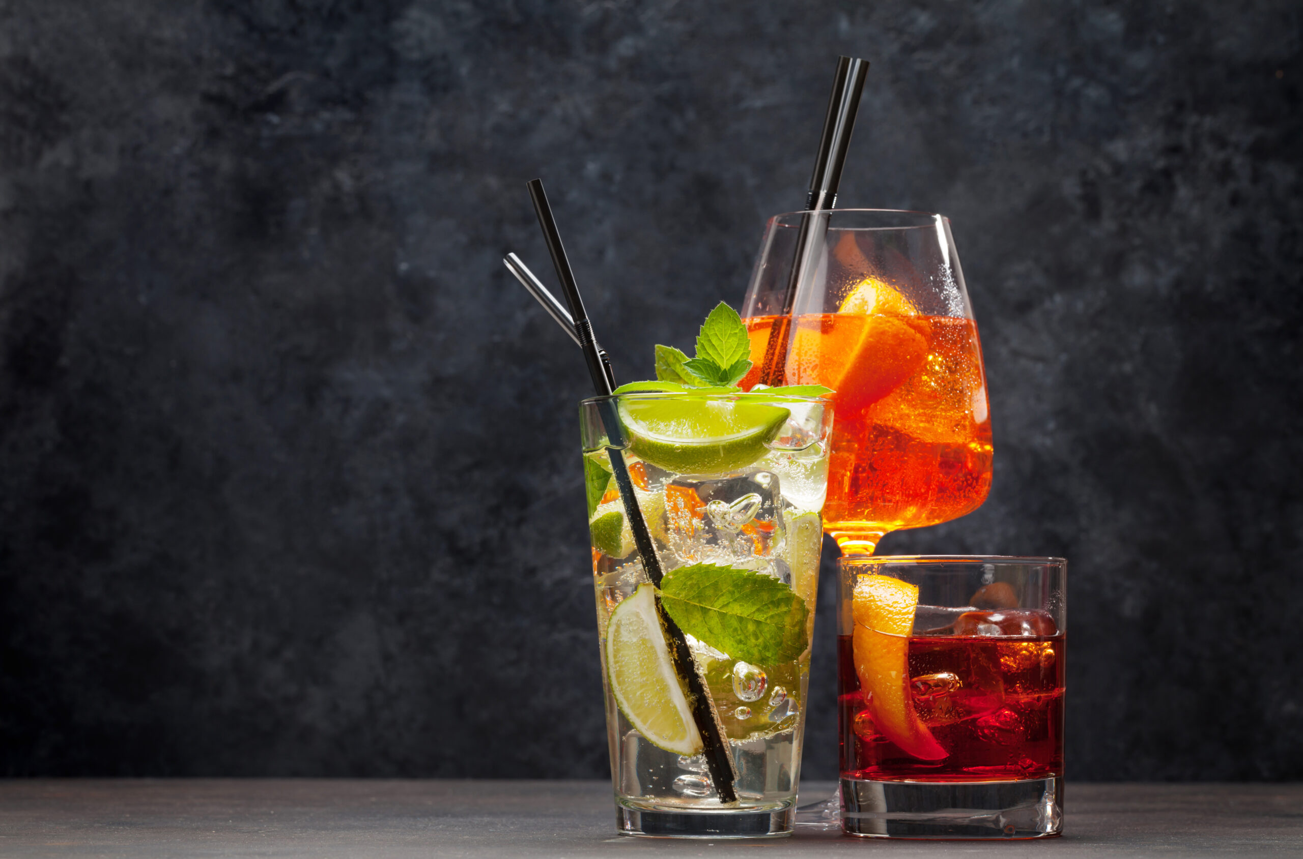 Three classic cocktail glasses on wooden table. Negroni, aperol spritz and mojito. With copy space